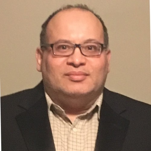 Nadir Doctor wearing a dark blazer and a beige collared shirt.